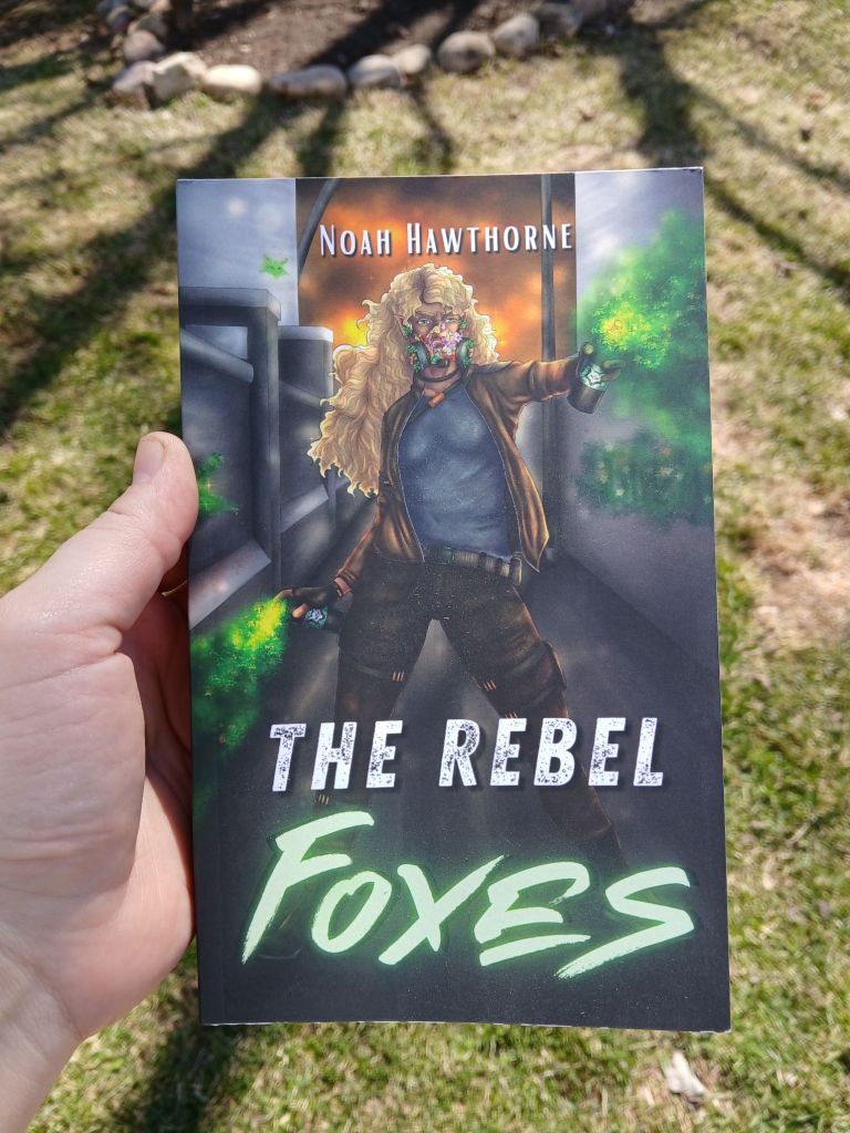 A paperback copy of The Rebel Foxes held up in front of a partially green lawn.

The cover of The Rebel Foxes by Noah Hawthorne.

A woman with brown skin and long curly blonde hair stands defiantly in the center. She wears a leather jacket, tight pants, and a gas mask full of plants. She sprays magical green spray paint to the left and right across a stone corridor. She has a determined look on her face.